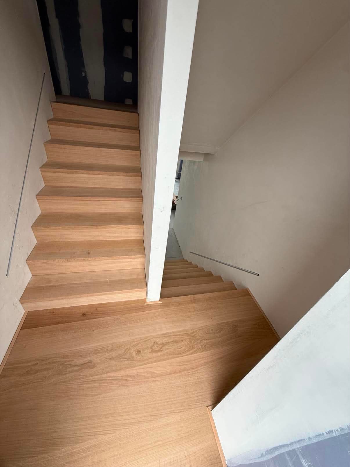 Escalier intérieur en chêne clair vu depuis le palier, avec une fine main courante métallique fixée au mur.
