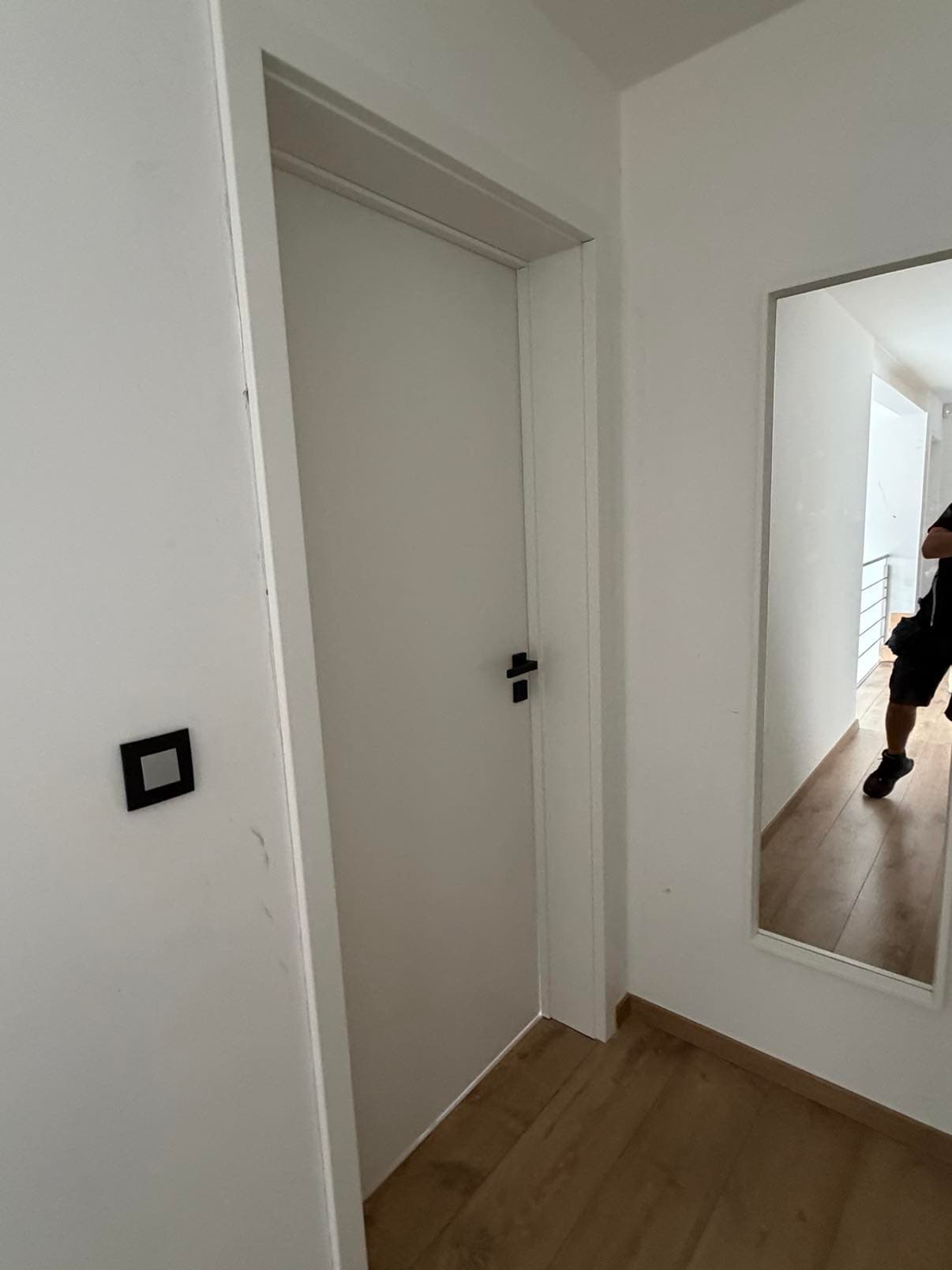 Porte intérieure blanche à poignée noire et grand miroir encadré de blanc, dans un couloir au sol en parquet.
