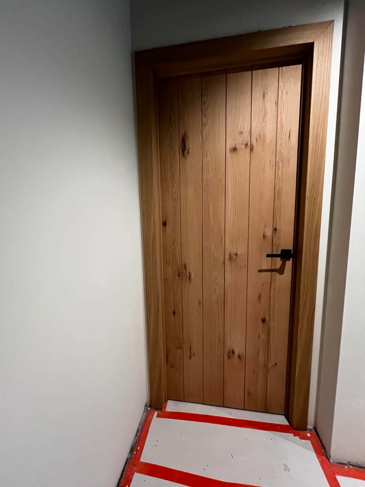 Porte intérieure en chêne massif à larges lames verticales, avec son bâti en chêne et une poignée noire.