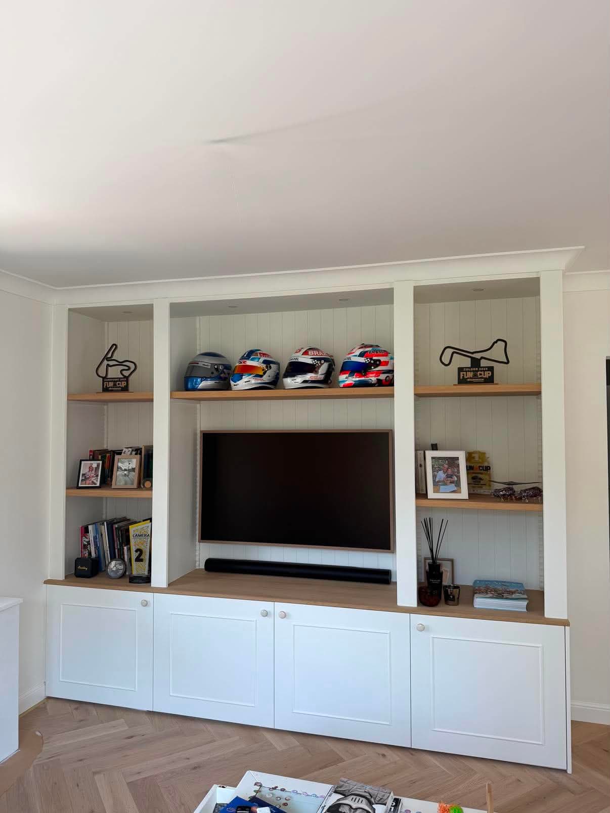 Meuble de séjour blanc toute hauteur avec niches, tablettes en chêne, téléviseur encastré et portes fermées en partie basse.