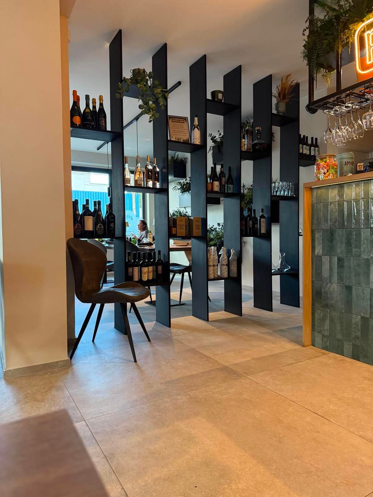 Cloison ajourée en panneaux noirs formant des étagères à bouteilles, séparant deux salles d'un bar à vin.