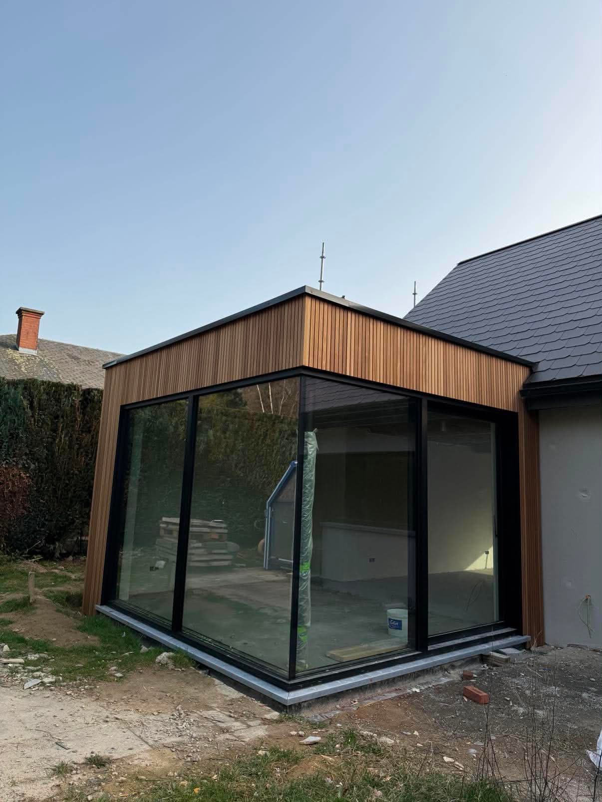 Extension de maison en construction, à grandes baies vitrées d'angle et bardage en bois vertical.