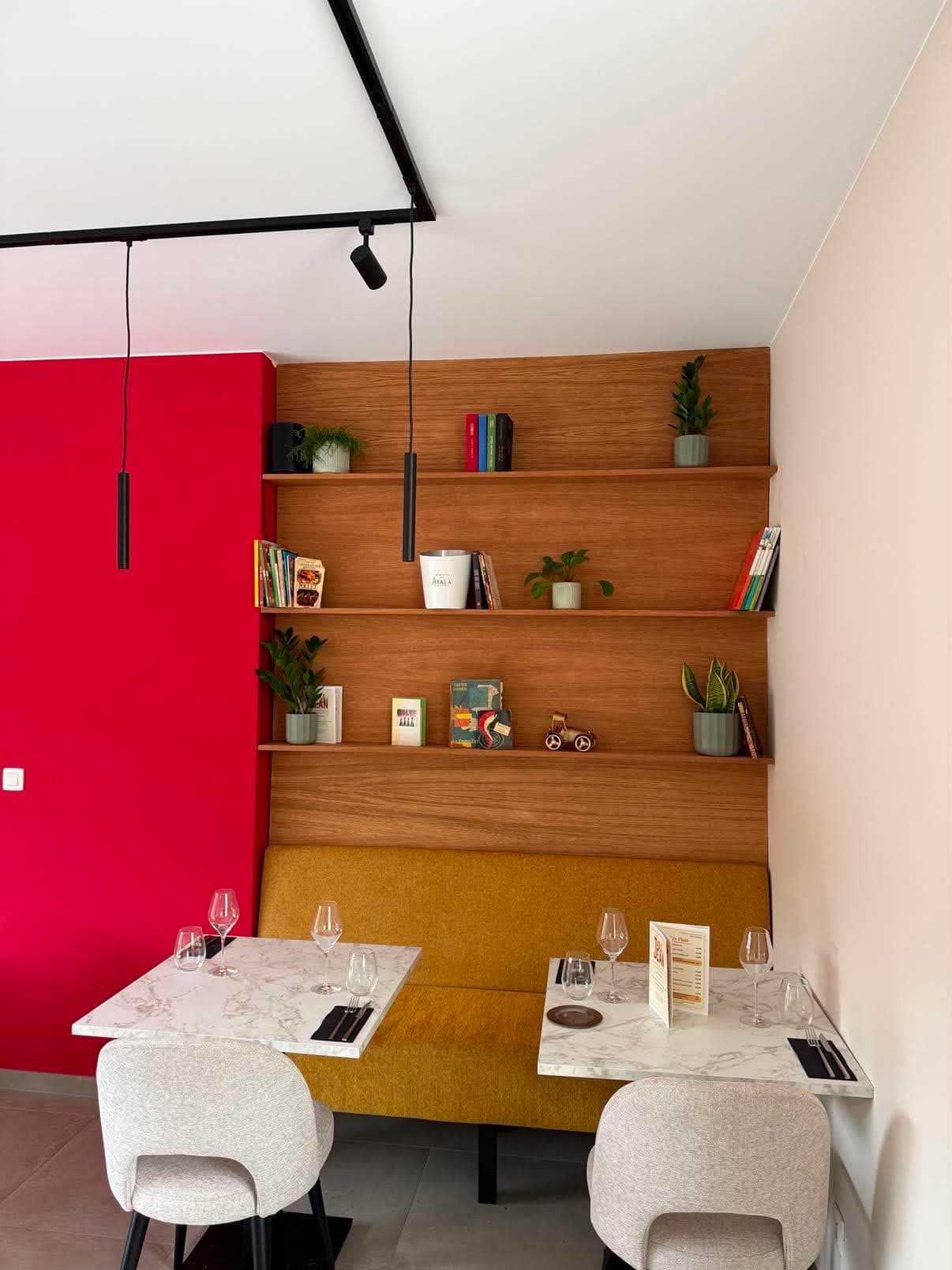 Banquette de restaurant adossée à un panneau de chêne garni d'étagères, devant deux tables en marbre.