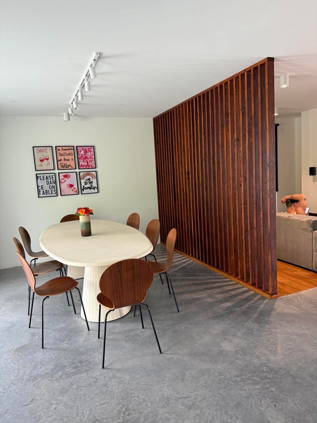 Cloison claustra en tasseaux de noyer séparant une salle à manger d'un salon, projetant son ombre sur le sol en béton ciré.