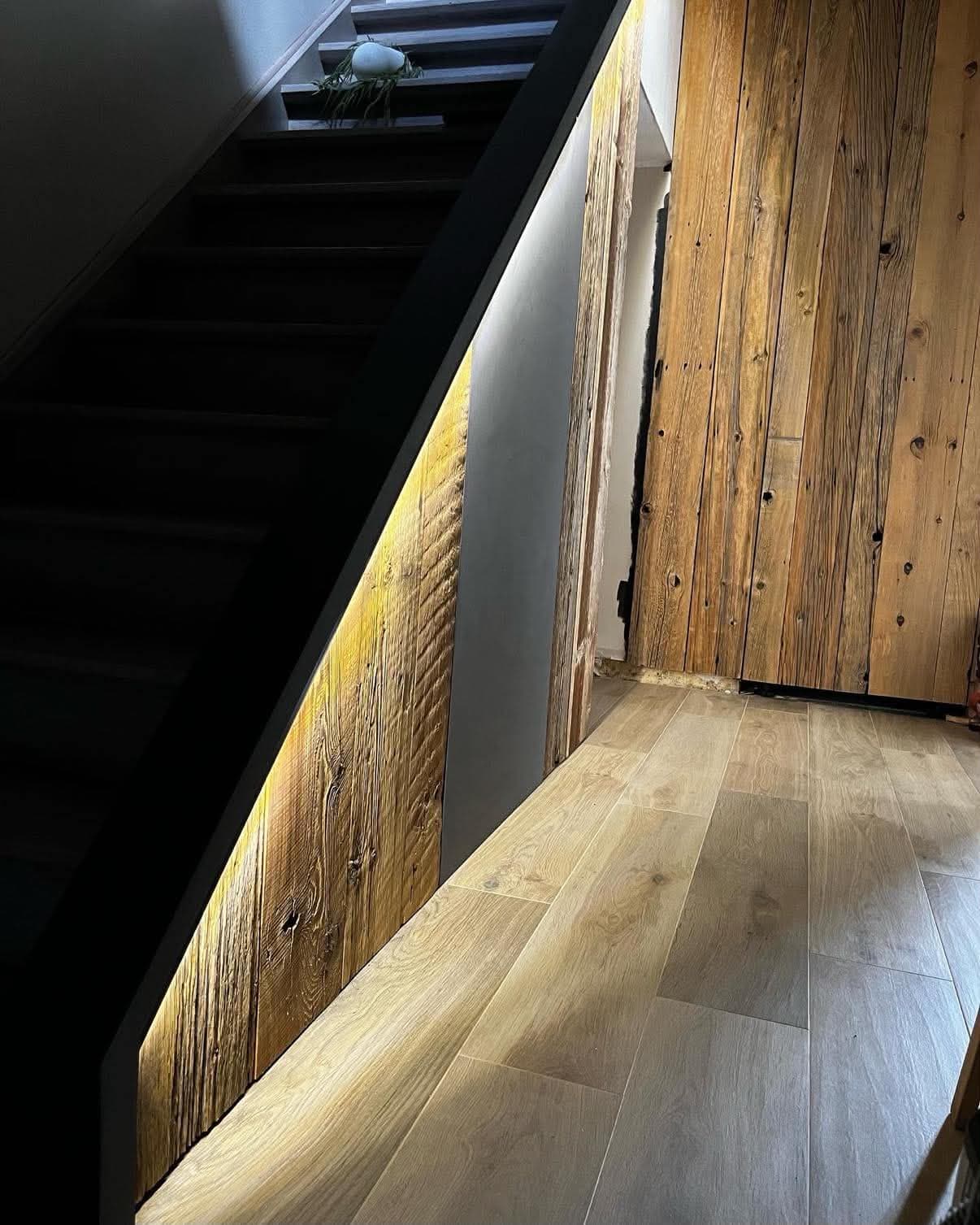 Habillage de sous-escalier en planches de vieux bois souligné par un éclairage LED, ouvrant sur une cloison assortie.