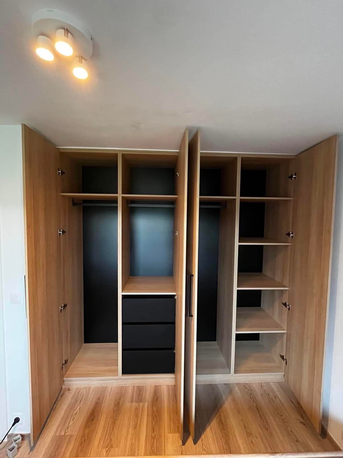 Dressing de chambre en panneau décor chêne, portes ouvertes sur une penderie, des tiroirs noirs et des colonnes d'étagères.