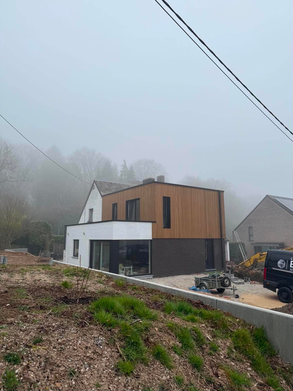 Maison en rénovation dont l'étage est habillé d'un bardage en lames de bois verticales, un matin de brouillard.
