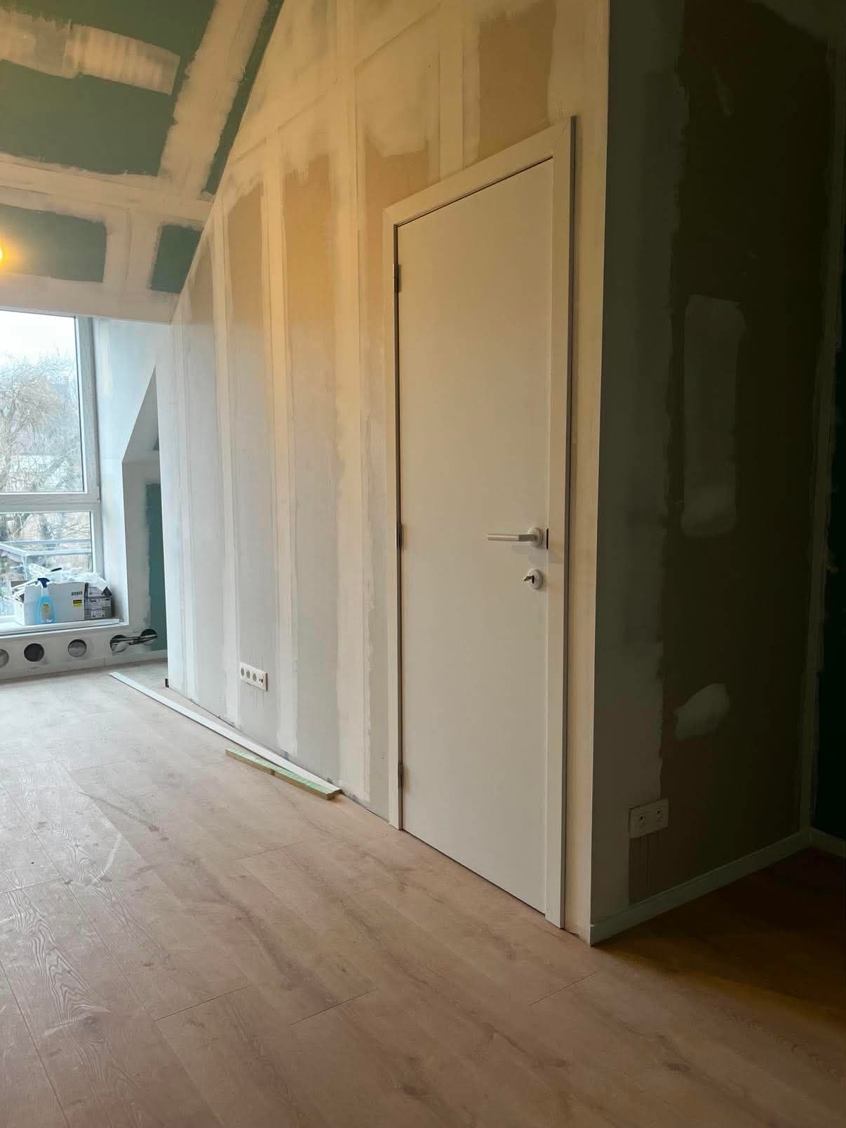 Cloison en plaques de plâtre montée sous rampant avec sa porte blanche, dans des combles en cours d'aménagement.