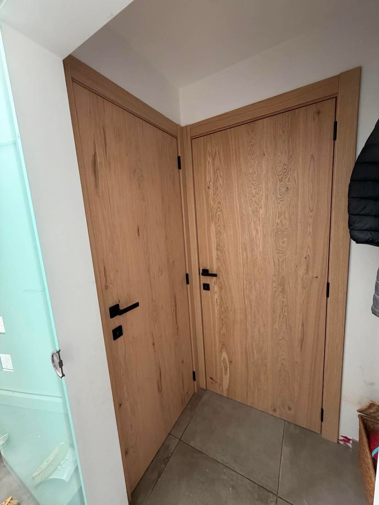 Deux portes intérieures en placage de chêne posées dans l'angle d'un hall, avec bâtis assortis et poignées noires.