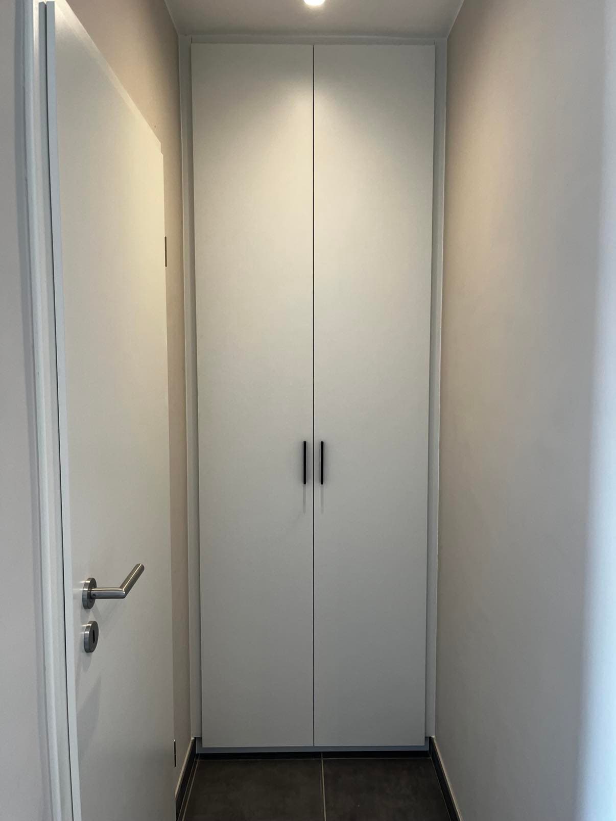 Placard blanc toute hauteur à deux portes et poignées noires, encastré dans un couloir étroit.