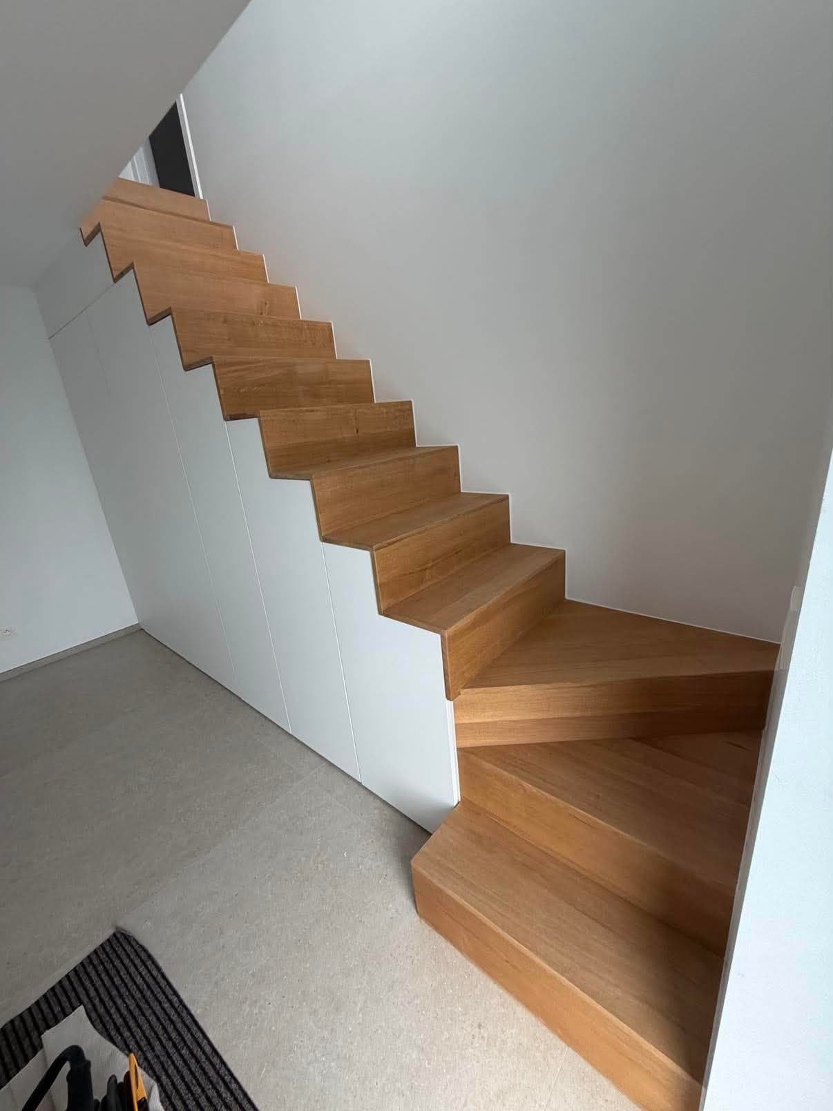 Escalier quart tournant en chêne massif dont le dessous est fermé par des placards blancs sans poignées.