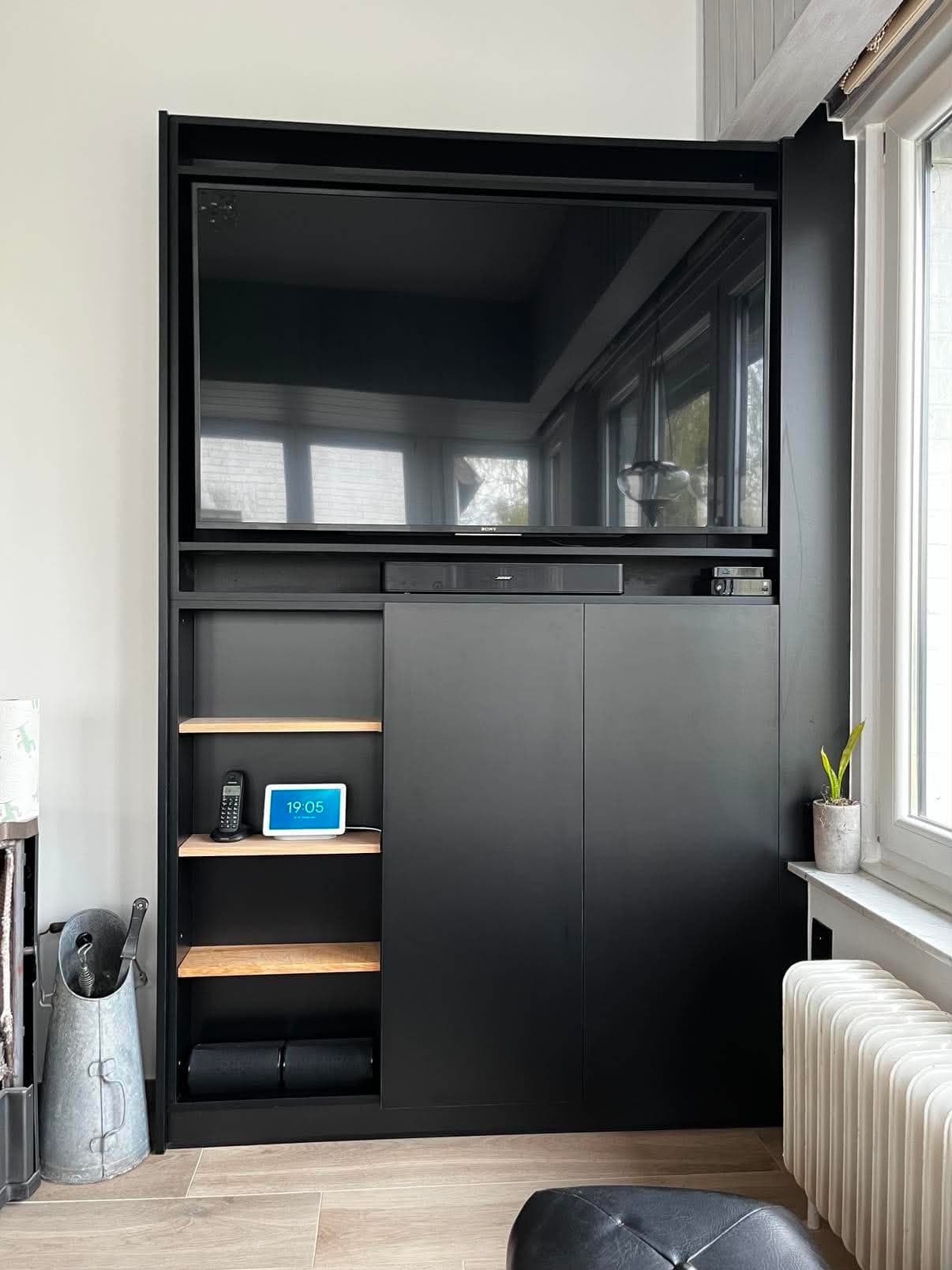 Meuble de séjour noir mat encastré entre deux murs, avec téléviseur, tablettes en chêne et portes coulissantes.