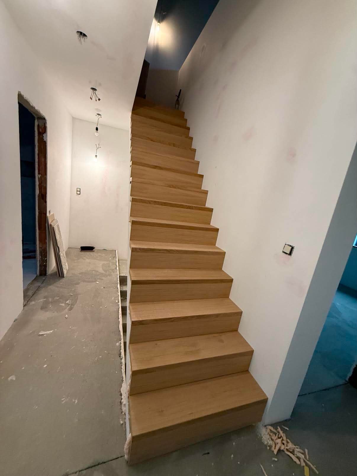 Escalier droit en chêne massif fraîchement posé dans une cage d'escalier encore en chantier.