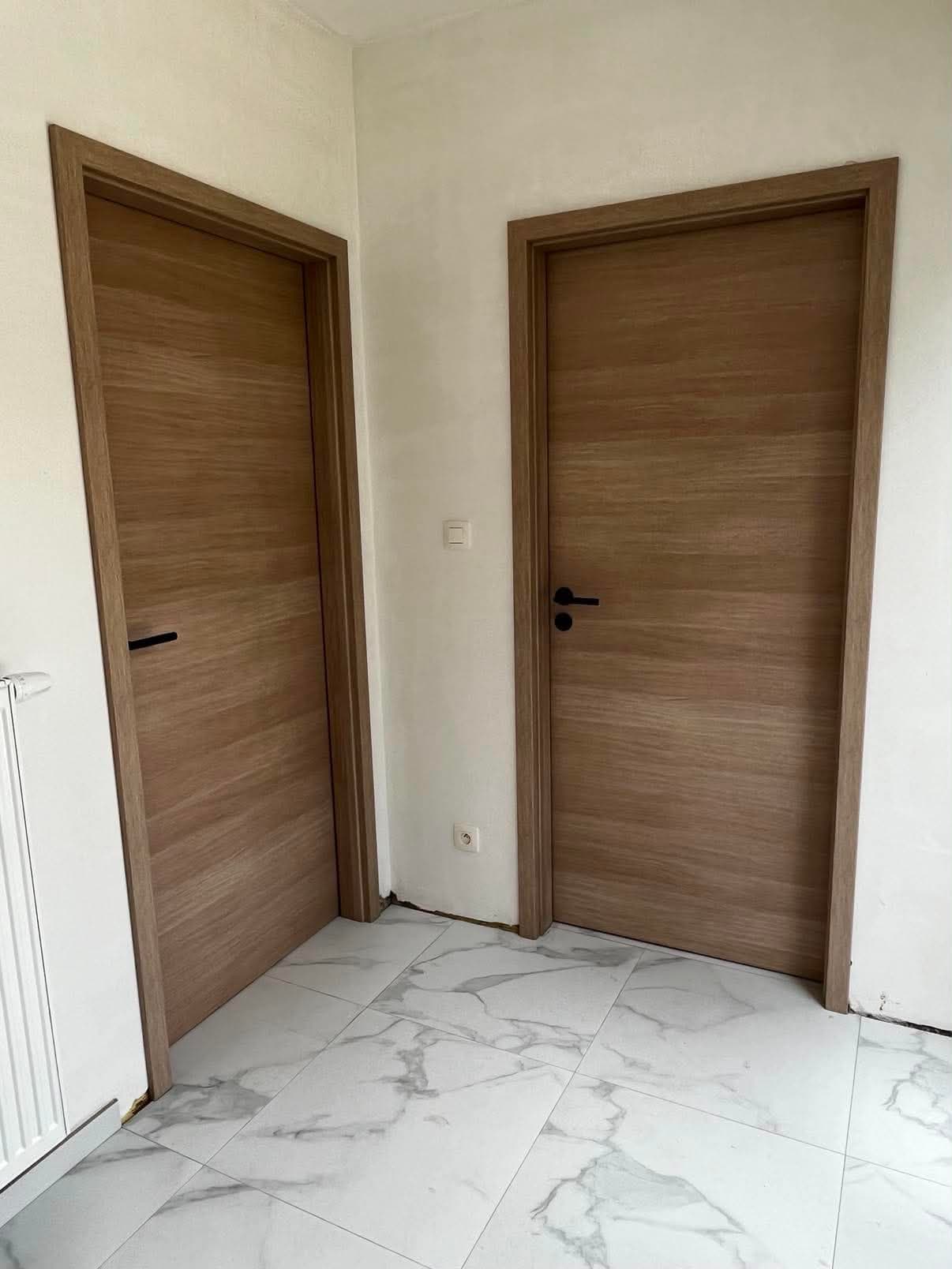 Deux portes intérieures en placage de chêne teinté avec leurs bâtis, dans une pièce au sol en marbre blanc.