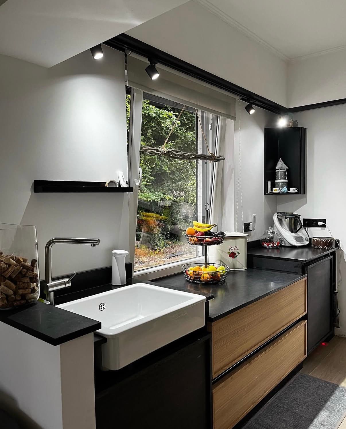 Cuisine sur mesure aux façades en chêne, plan de travail en pierre noire et évier de ferme en céramique blanche.